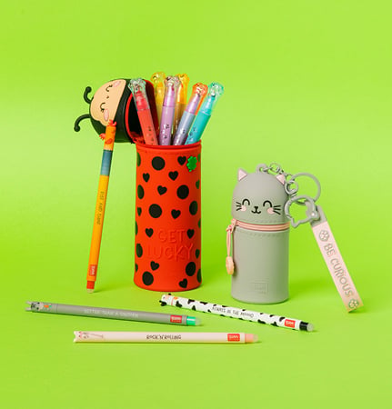Fotografia ufficiale Legami con astuccio coccinella, portamonete con portachiavi Kitty e penne colorate su fondo verde.